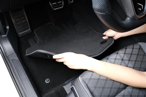 Hands securing a car mat in place to prevent sliding on the driver’s side floor